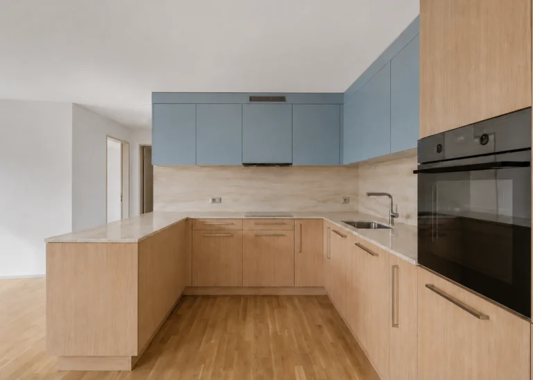 Cuisine en U vue depuis le séjour, four noir encastré, plan en travertin, parquet clair