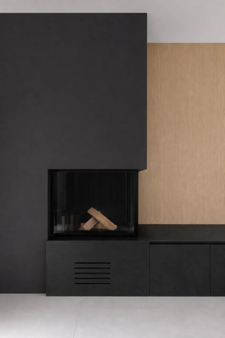 Cheminée à habillage noir mat adossée à un rangement toute hauteur en bois clair