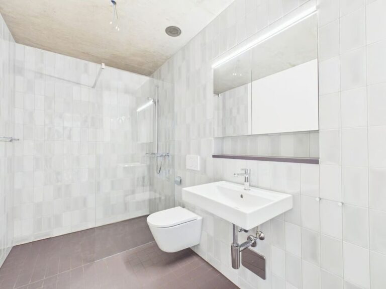 Salle de bain rénovée en carrelage blanc avec douche vitrée et plafond béton