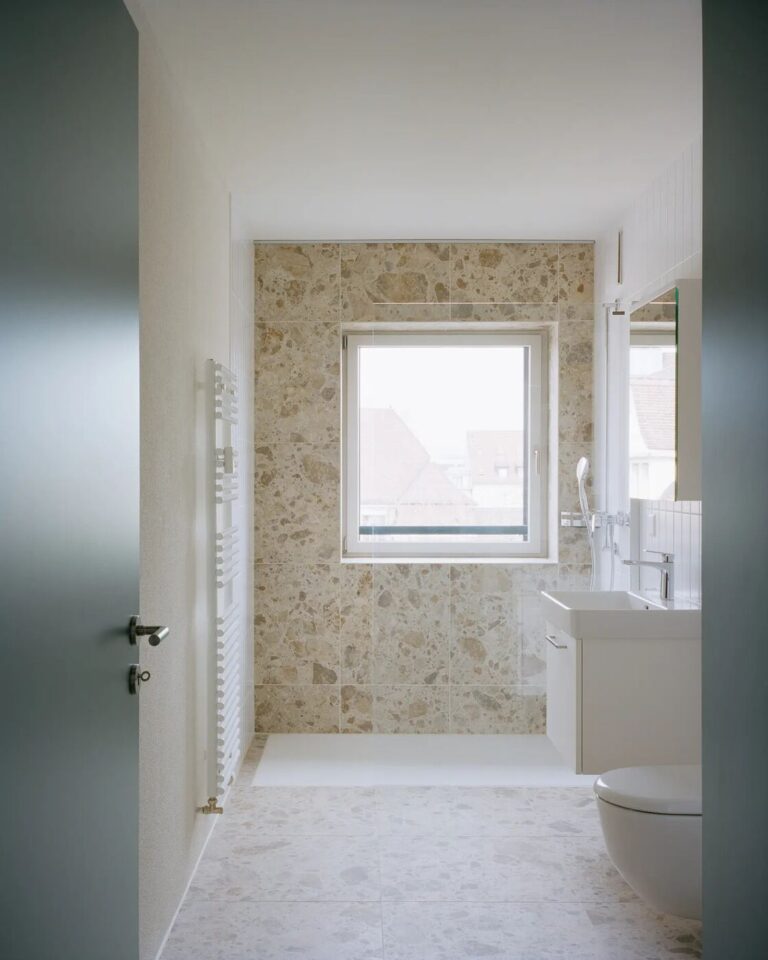 Salle de bain rénovée avec douche à l’italienne et mur en terrazzo beige