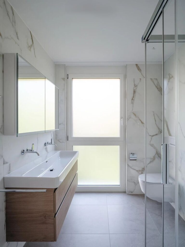 Salle de bain rénovée en marbre blanc avec grande vasque et meuble en bois