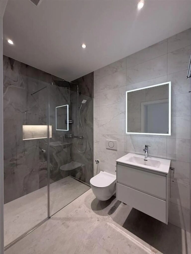 Salle de bain rénovée en marbre gris avec douche à l’italienne et miroir rétroéclairé